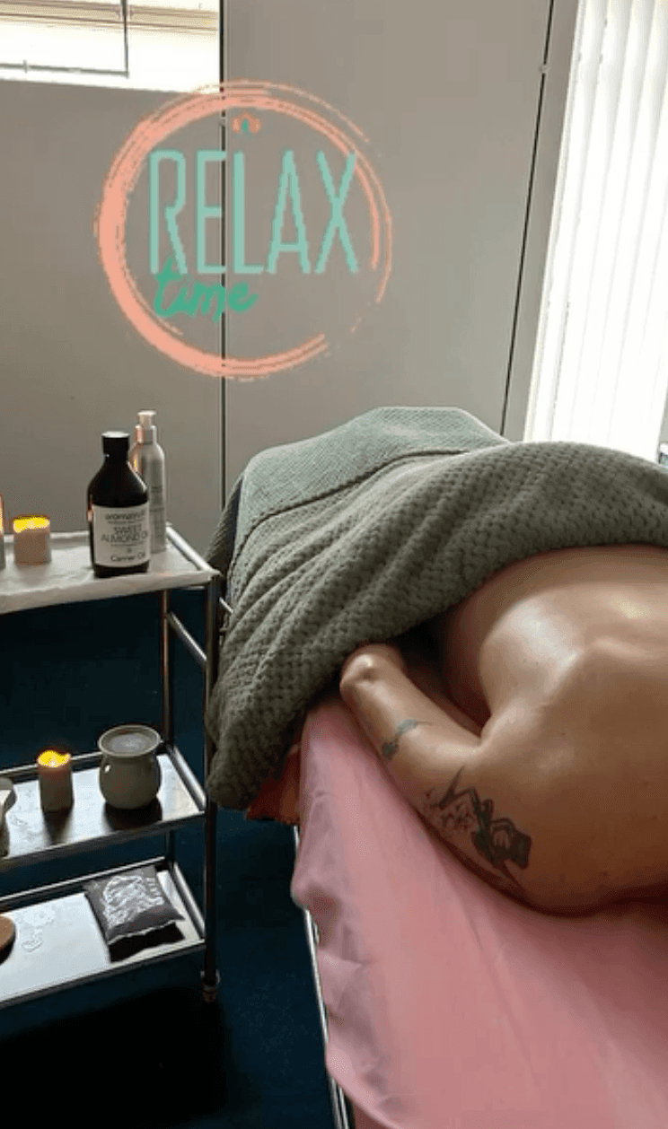 Person lying under a blanket on a massage table with candles and oils nearby.